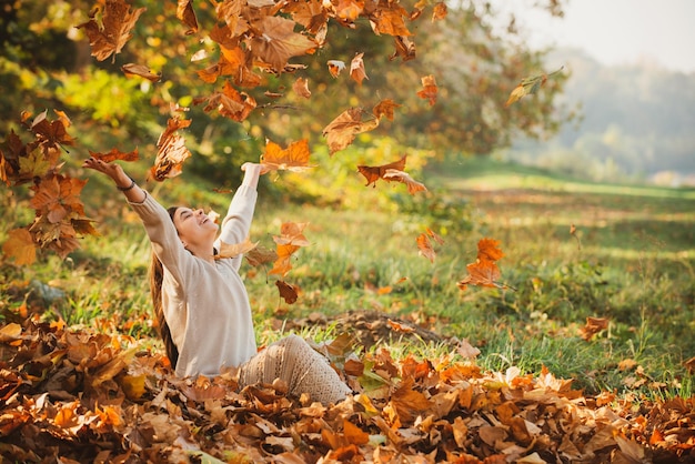 Autumn leaves falling on happy young woman in forest The colors and mood of autumn Beautiful young woman throwing leaves in a park Fall concept Happy smiling girl with natural red hair