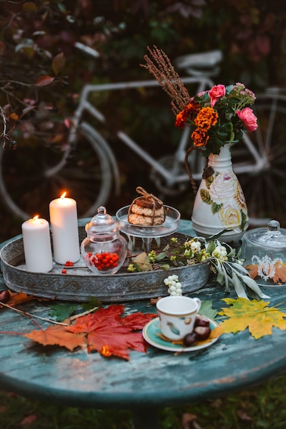 Autumn leaves lie on a wooden antique round table with crockery cups and cookies burning candle.