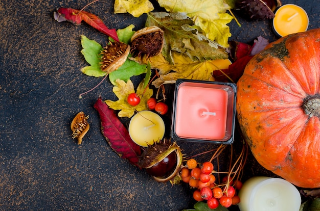 Autumn leaves, pumpkin, chestnuts, candles on a dark background