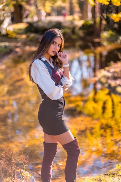 Autumn lifestyle, a young Caucasian brunette, college girl in a fashionable pose, in a park by a lake