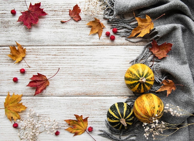 Photo autumn maple leaves pumpkins and woolen scarf on a wooden background