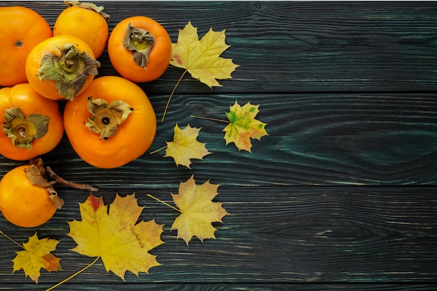 Autumn maple leaves and ripe persimmons on a textured wooden background