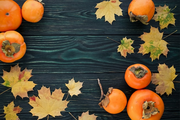 Autumn maple leaves and ripe persimmons on a textured wooden background