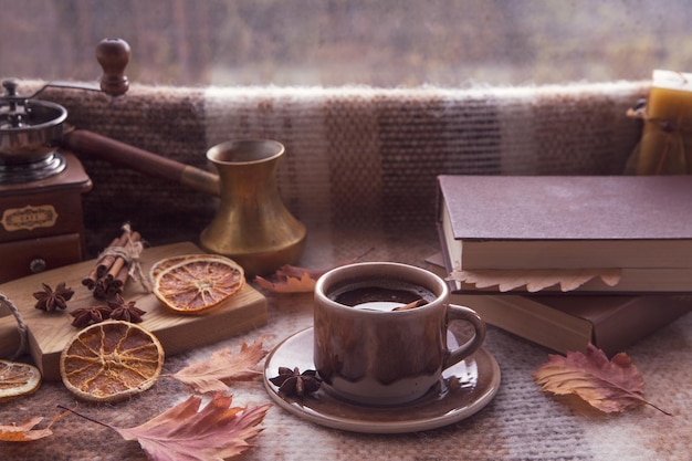 Autumn mood autumn atmosphere A cup of hot coffee cinnamon sticks star anise a book autumn leaves on a knitted plaid on a rainy day