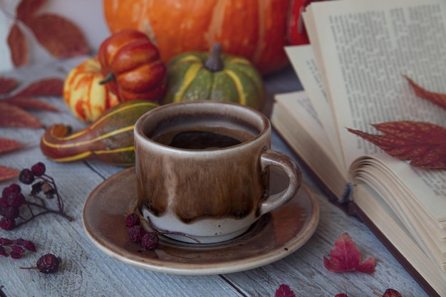 Autumn mood autumn background A cup of hot coffee an open book autumn leaves berries and pumpkins on a wooden table Thanksgiving Day