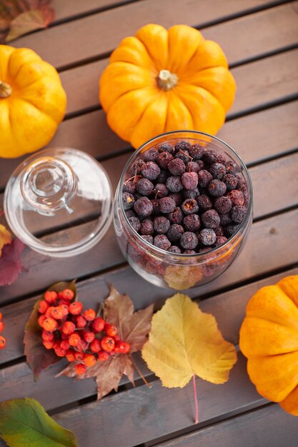 Autumn mood composition on a grey wooden table with pumpkins, rowan and leaves. Glass open jar with dried hawthorn for tea