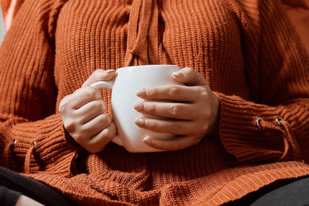 Autumn mood young female in orange woolen pullover drinking refreshing coffee in a cold autumnal mor...