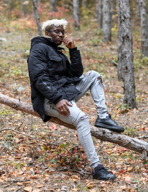 Autumn nature with human young african american man resting in the forest sitting on a fallen tree