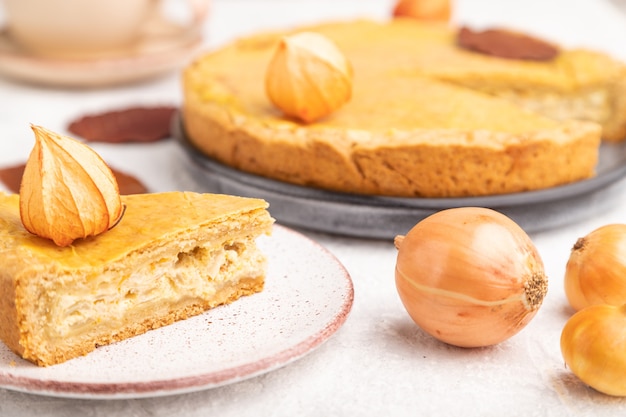 Autumn onion pie decorated with leaves and cup of coffee on gray concrete