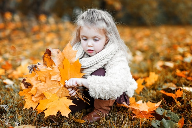 Autumn outdoor portrait of a happy child with yellow leaves in the park