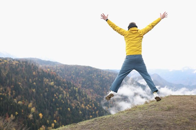 Autumn panoramic view and jumping tourist with open arms on top of mountain