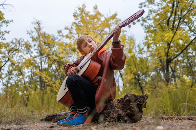 In autumn in the park a boy plays the guitar looks at the strings and tunes the guitar