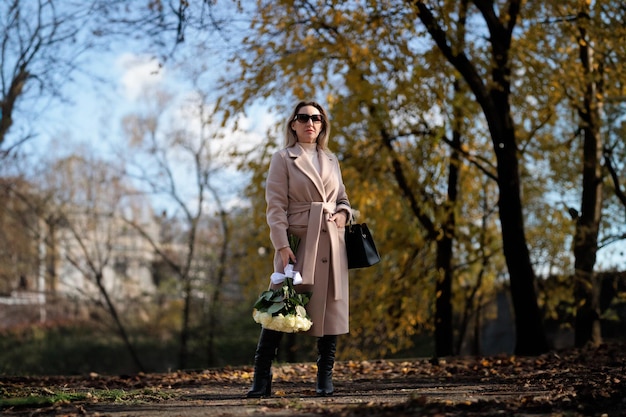 In the autumn park a business woman is holding a bouquet of white roses