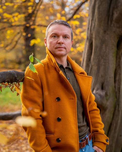 Autumn photography Beautiful colors of autumn A man in a yellow coat and blue jeans near a tree Yellow foliage Calm thoughtfulness Reasoning Dream LonelinessAutumn look