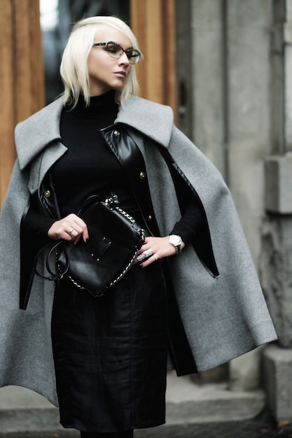 Autumn portrait of beautiful blonde woman in grey coat with black bag