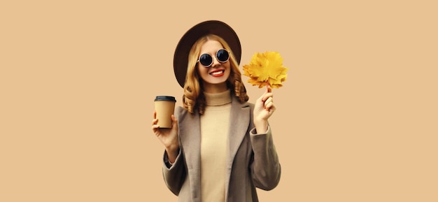 Autumn portrait of beautiful smiling young woman with yellow maple leaves and cup of coffee