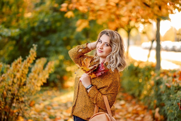 Autumn portrait of a plus size girl with a bouquet of yellow leaves in her hands Stylish woman in the autumn park