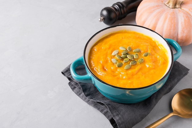 Autumn pumpkin soup with foliage and raw pumpkin