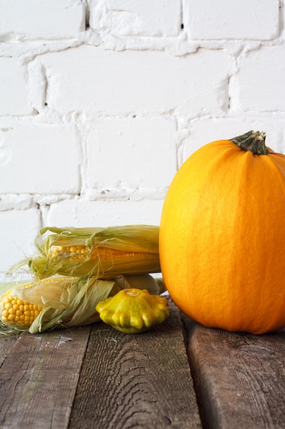 Autumn pumpkins and other vegetables on a wooden table, white brick backdrop