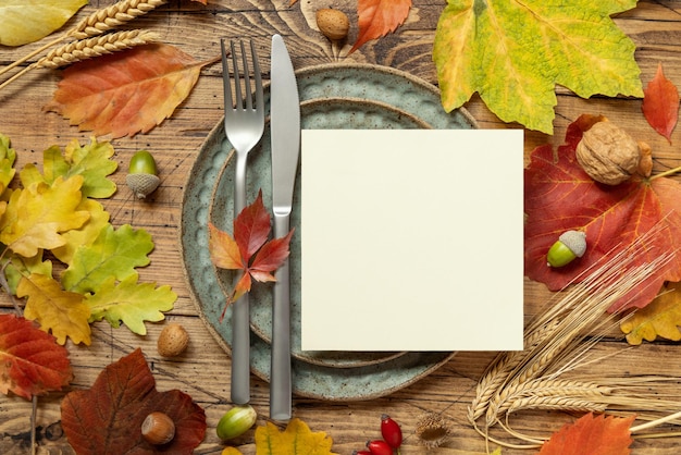 Autumn rustic table setting with red yellow and orange leaves berries and blank card top view mockup