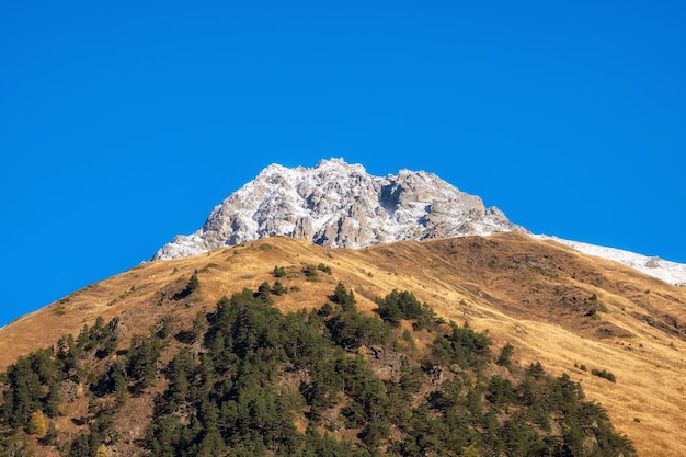 Autumn snow mountains at noon Bright mountain landscape with a snowy rock in golden sunlight Natural background of a walk through the rocky mountains with sharp rocks and blue sky