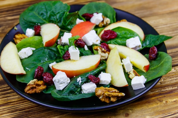 Autumn spinach salad with apple feta cheese walnut and dried cranberry on wooden table Healthy vegetarian food