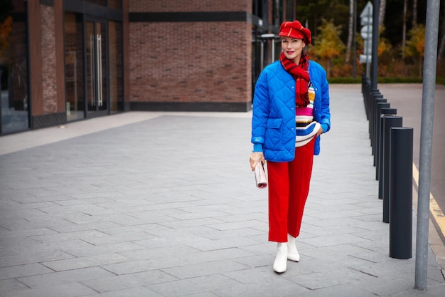 Autumn or Spring street style trend Clothes. Bright outfit for woman. Model wearing blue jacket, red pants and vibrant accessories beret or hat, scarf. Copy space