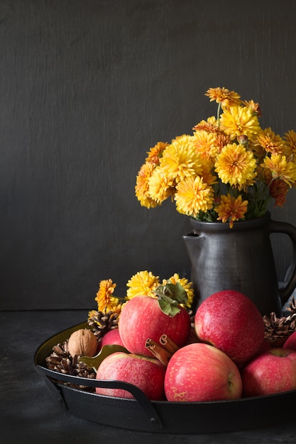 Autumn still life. Fall harvest with apples, yellow flowers in vase on dark.