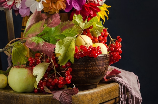 Autumn still life with apples, viburnum berries, autumn leaves on a vintage wooden chair on a black surface