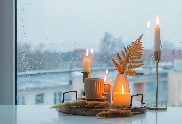 autumn still life with burning candles and a cup of coffee on the background of a window with raindrops