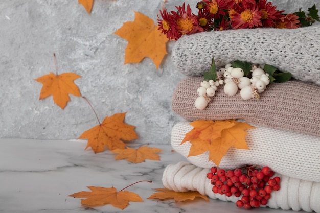 Autumn still life with knitted sweaters fallen leaves pumpkins and mountain ash