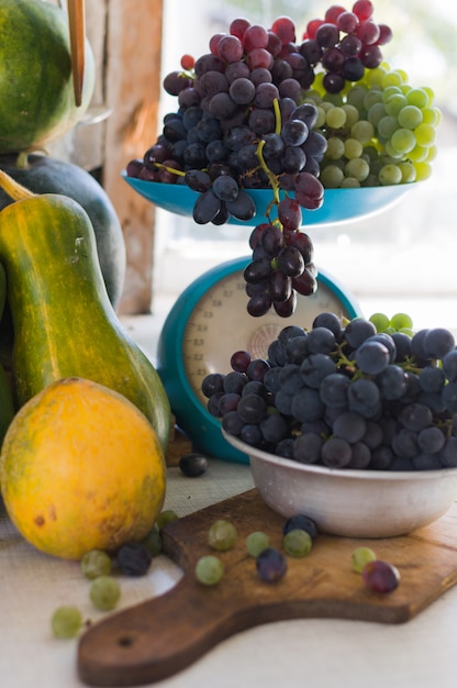 Autumn still life with pumpkins, and grapes on the scales and in a metal bowl on a wooden white table. Autumn harvest concept.