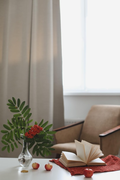 Autumn still life with a rowan branch in a vase book and apples in a cozy home interior