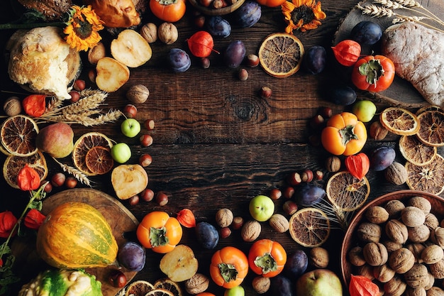 Autumn stilllife composition with fresh fruits and vegetables Assortment of plums persimmon pumpkins apples walnut sunflowers and dry oranges on rustic wooden table top view copy space