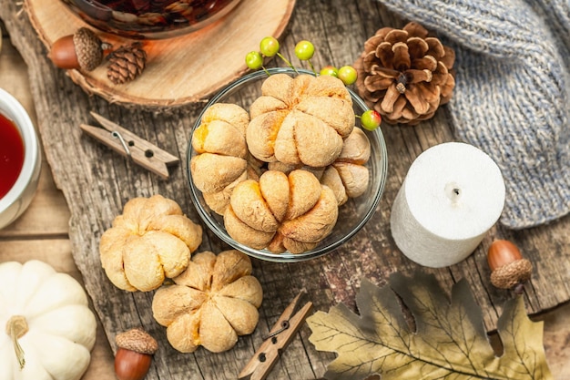 Autumn tea concept. Cookies with pumpkin puree, black tea in a glass teapot, fall decor. Wreath, candles, a cozy sweater. Old wooden background, close up