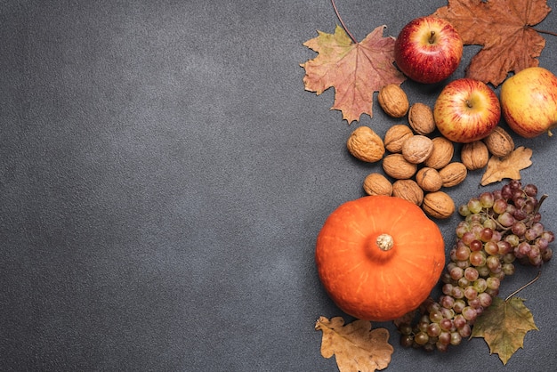 Autumn vegetables fruits nuts and dry leaves on black background