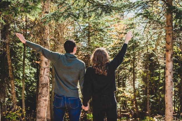 Autumn Walk in the forest. Rear view of couple stands with arms outstretched. Man and woman in warm clothing are happy.