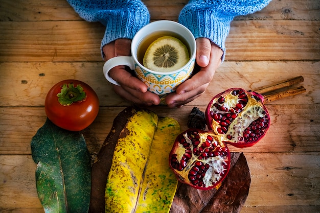 Autumn and winter cold concept image with top view of wooden rustic table and people hands holding a hot cup of tea