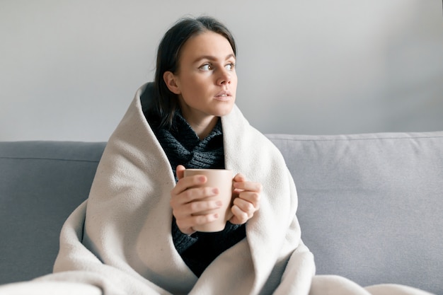 Autumn winter portrait of young girl with cup of hot drink, under warm blanket