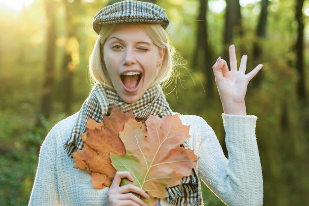 Autumn woman. Happy autumn girl wink. Cheerful carefree autumn woman in park on sunny day. Girl