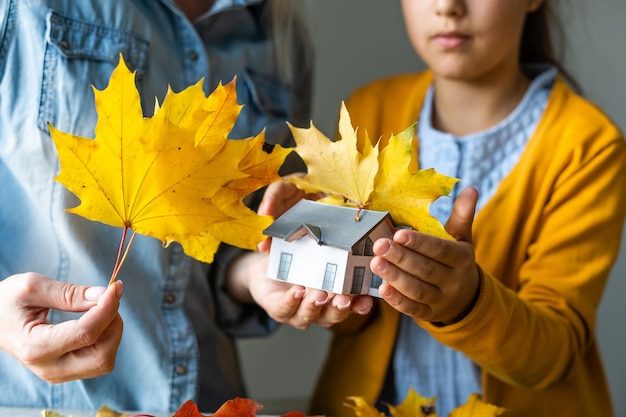 Autumnal Background. Toy house and dried orange fall maple leaves. Thanksgiving banner copy space. Hygge mood cold weather concept. Hello Autumn with family.