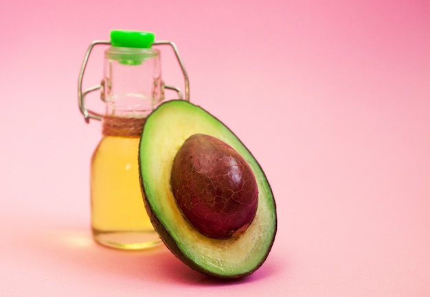 Avocado and avocado oil in bottle on pink background.