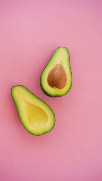 Avocado cut in halves on pink surface