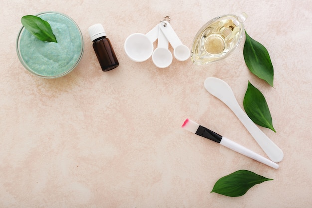 Avocado face mask, spatula, brush, measuring spoons, oil, essential oil on light pink background