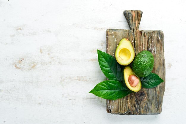 Avocado and green leaves on a white wooden background Rustic style Top view Free space for your text