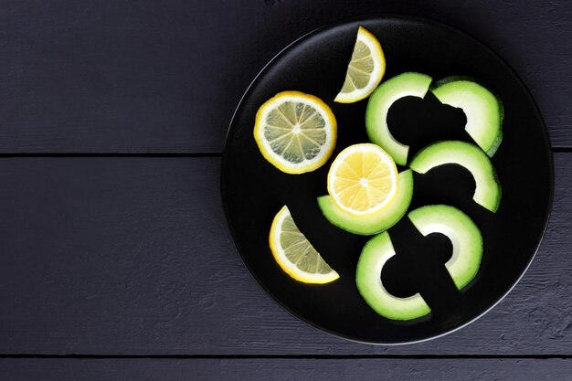 Avocado and lemon on black plate Sliced avocado and lemon on black wooden boards Vegetarian food Copy space