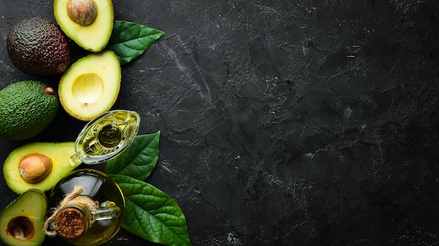 Avocado oil and fresh avocados on a black background Rustic style Top view Free space for your text