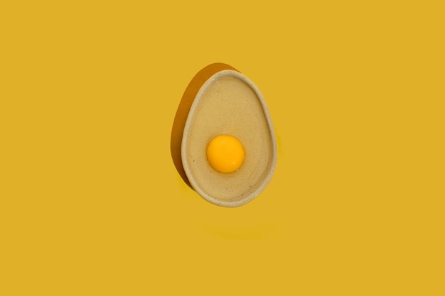 Avocado shaped ceramic plate with raw egg yolk on a bright yellow color background with copy space Healthy dieting idea