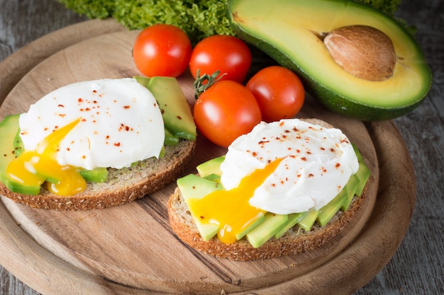 Avocado toast, cherry tomato and poached eggs on wooden . Breakfast with vegetarian food, healthy diet .