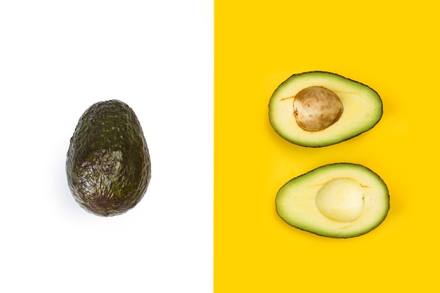 An avocado and two half on a yellow and white background